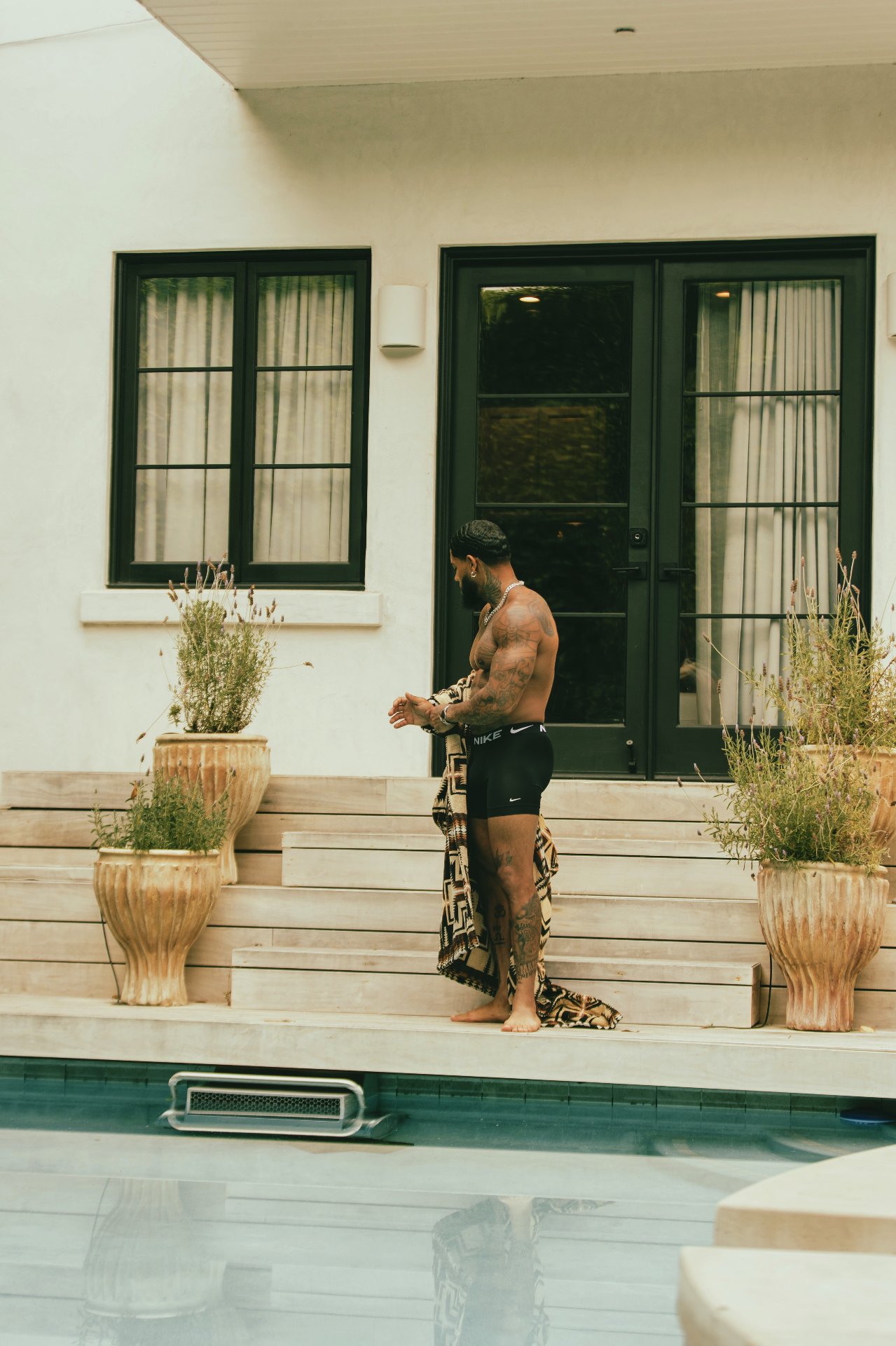 Fredo standing poolside by a black-framed doorway